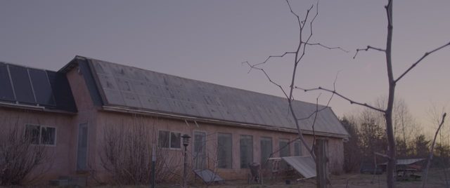 The main building at Living Energy Farm at dusk: a long earthen wall under a roof of solar panels.